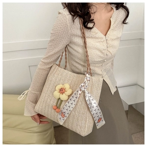 Detail of hand-woven straw tote with floral pendant and patterned silk scarf handle