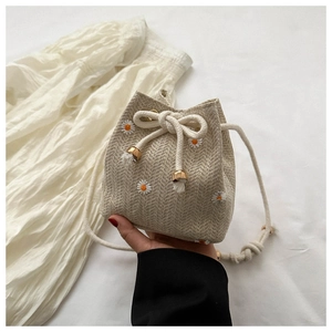 Close-up of woven bucket bag featuring white daisy embroidery and drawstring detail