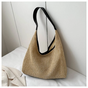 Détail du sac hobo en paille tressée montrant la bordure en cuir noir et la bandoulière