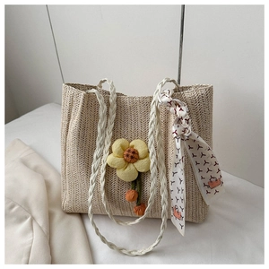 Detail of straw woven tote bag featuring a yellow flower charm and silk scarf handle