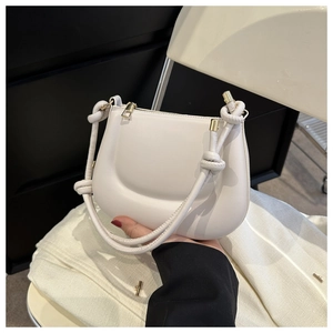 Detail of minimalist cream saddle bag featuring leather texture and gold knot hardware