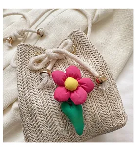 Close-up of beige woven bucket bag with pink fabric flower and gold drawstring tips