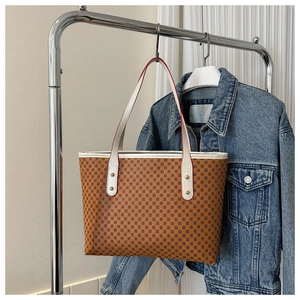 Detail of a brown tote bag with pattern print, white leather straps and rivet accents