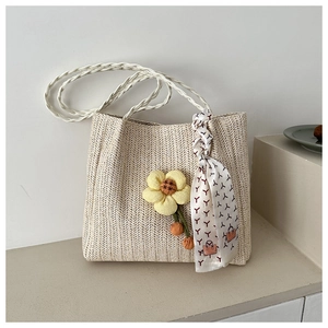 Close-up of beige straw tote bag featuring a yellow flower charm and silk scarf detail