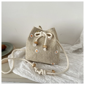 Detail of woven bucket bag featuring white daisy embroidery and drawstring closure