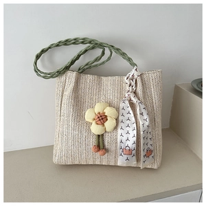 Detail of woven straw tote bag featuring green straps and decorative yellow floral accent