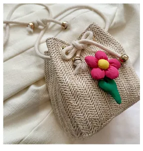 Close-up of woven straw bucket bag with red fabric flower and beige drawstring closure