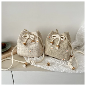 Detail of hand-woven straw bucket bags with embroidered daisy patterns and drawstring closure