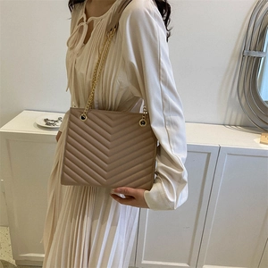 Elegant apricot V-quilted tote bag with gold chain strap worn by a female model