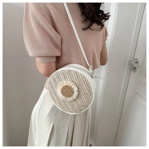 Détail d'un sac bandoulière rond en paille tissée avec fleur de marguerite en relief