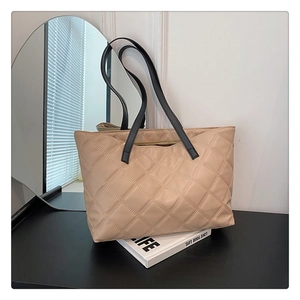 Close-up of a beige quilted tote bag with black shoulder straps on a modern desk setup