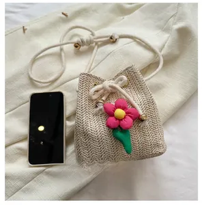 Detail of straw bucket bag with floral decor and drawstring next to phone for size