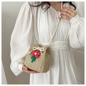 Detail of hand-woven straw bucket bag with cotton drawstring closure and floral charm