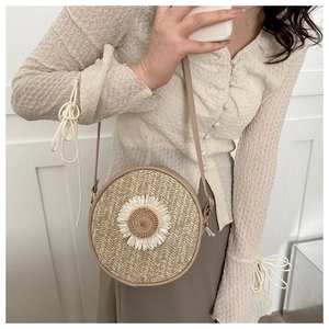 Détail d'un sac bandoulière rond en paille avec des décorations de marguerites blanches
