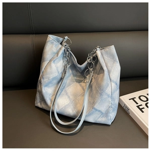 Details der hellblauen Stepp-Tasche mit silberner Kette auf einem grauen Ledersessel