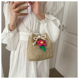 Detail of hand-woven straw bucket bag with floral accent and white drawstring closure