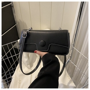 Close-up of black baguette bag with white contrast stitching and round decorative buckle