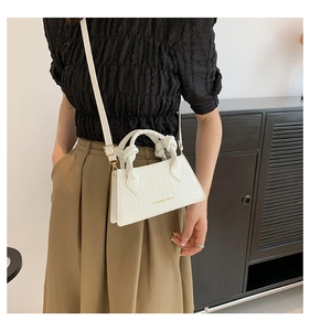 Détail du mini sac blanc texture crocodile avec texte doré et poignée nouée sur modèle