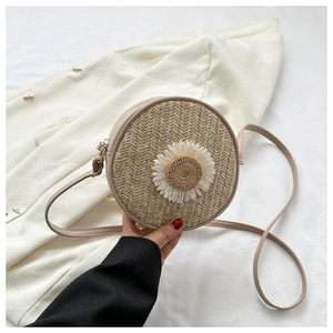 Détail du sac bandoulière rond en paille avec marguerite sur fond de blazer blanc
