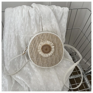 Détail d'un sac rond en paille tissée avec tournesol 3D et bandoulière blanche fine