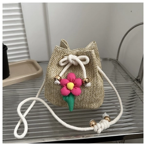 Detailed straw bucket bag featuring a large pink fabric flower and white drawstring cord