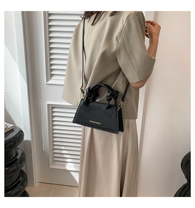 Détails d'un sac à main noir à texture croco, lettrage doré et poignées nouées