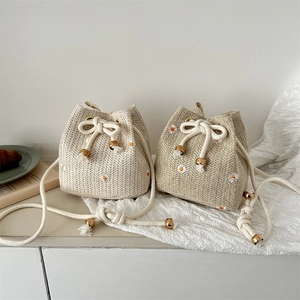 Handwoven straw bucket bags with daisy embroidery and drawstring closure in neutral tones