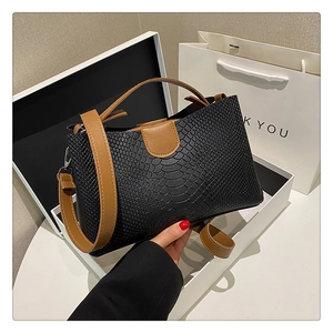 Detail of elegant black crocodile pattern tote bag with brown straps in a gift setting