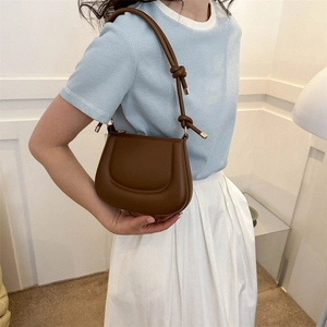 Brown leather saddle shoulder bag with textured seams worn by a model in a minimal studio