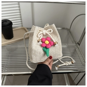 Detailed weave texture of straw bucket bag with pink floral charm and drawstring