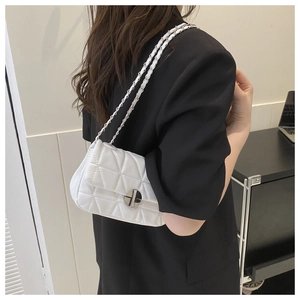 Close-up of white quilted chain bag with silver buckle worn by a model in a minimal room