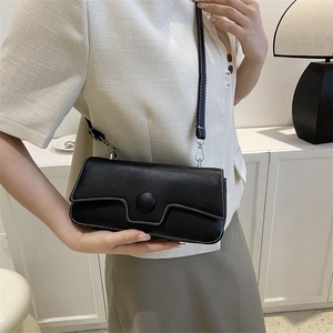 Minimalist black baguette bag with white contrast stitching and round buckle on a model
