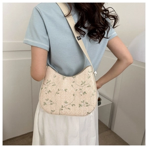 Detail of hand-woven straw bag featuring green floral embroidery and adjustable strap