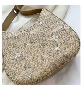 Detail of summer straw bucket bag with delicate floral embroidery and brown leather strap