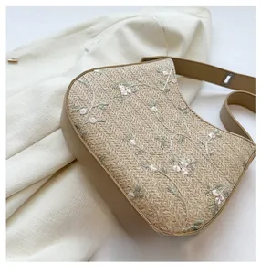 Detail of a straw bucket bag with floral embroidery and khaki leather trim accents