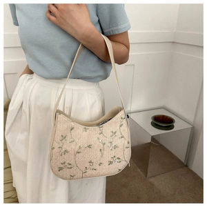 Detail of white straw shoulder bag featuring green floral embroidery and sequins