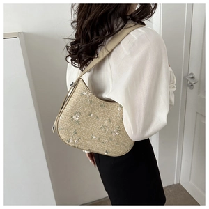 Detail of floral embroidery on a straw shoulder bag with creamy white leather strap
