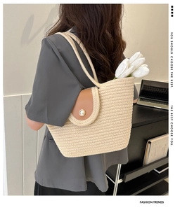 Detail of woven straw tote bag featuring brown leather flap and pearl button closure