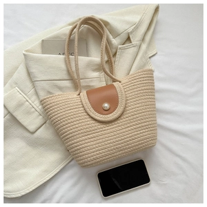 Detail of woven beach tote showing beige texture, leather flap, and pearl buckle decoration