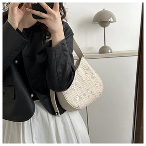 Detail of floral embroidery and woven texture on a cream straw shoulder bag