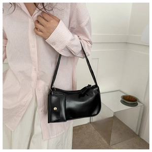 Detail of black glossy PU leather underarm bag with decorative bow and gold button