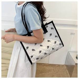 Detail of embroidered black rose patterns on white canvas tote bag with black handles