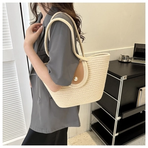 Detail of woven tote bag featuring a cream texture with brown leather flap and pearl buckle
