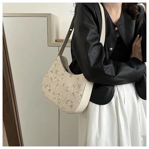 Detail of hobo straw shoulder bag featuring floral embroidery and cream leather trim