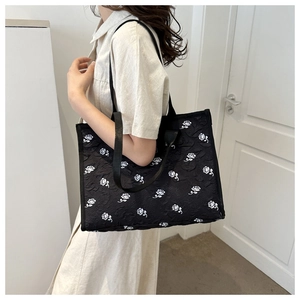 Detail of black tote bag with white 3D floral jacquard texture and wide shoulder strap
