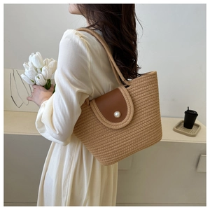 Close-up of woven tote bag featuring a brown leather lid and large pearl closure