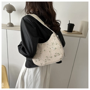 Detail of a beige woven shoulder bag with delicate green floral embroidery and moon shape