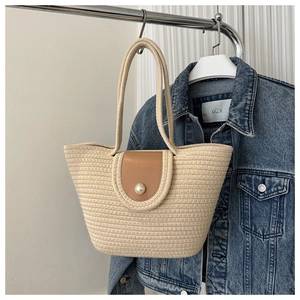 Detail of cream woven tote bag featuring brown faux leather flap and pearl closure