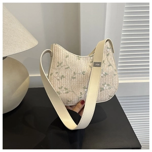 Detailed view of cream straw bucket bag featuring green floral embroidery and wide leather strap