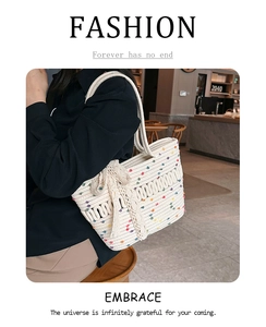 Detail view of a white woven tote bag with colorful specks and a large decorative bow